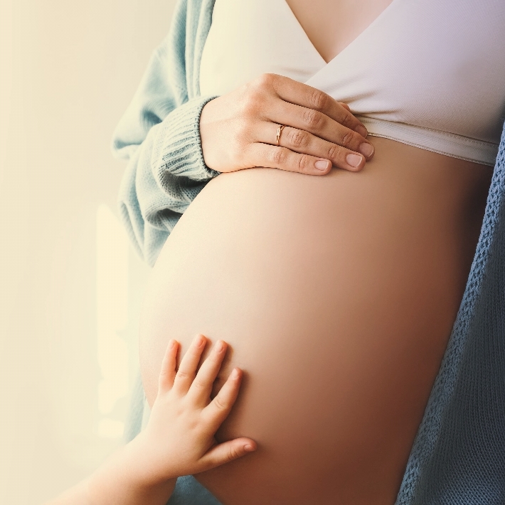 A mother's hand and a small child's hand resting on a pregnant belly